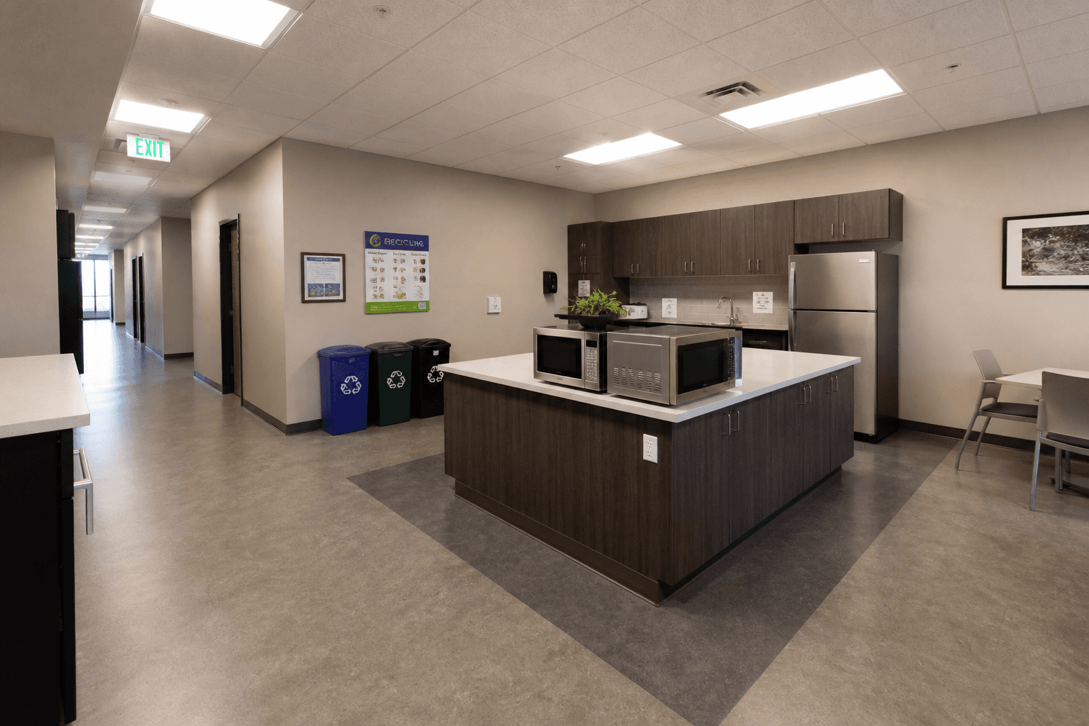Empty commercial break room and corridor junction with trash and recycling stations; no people