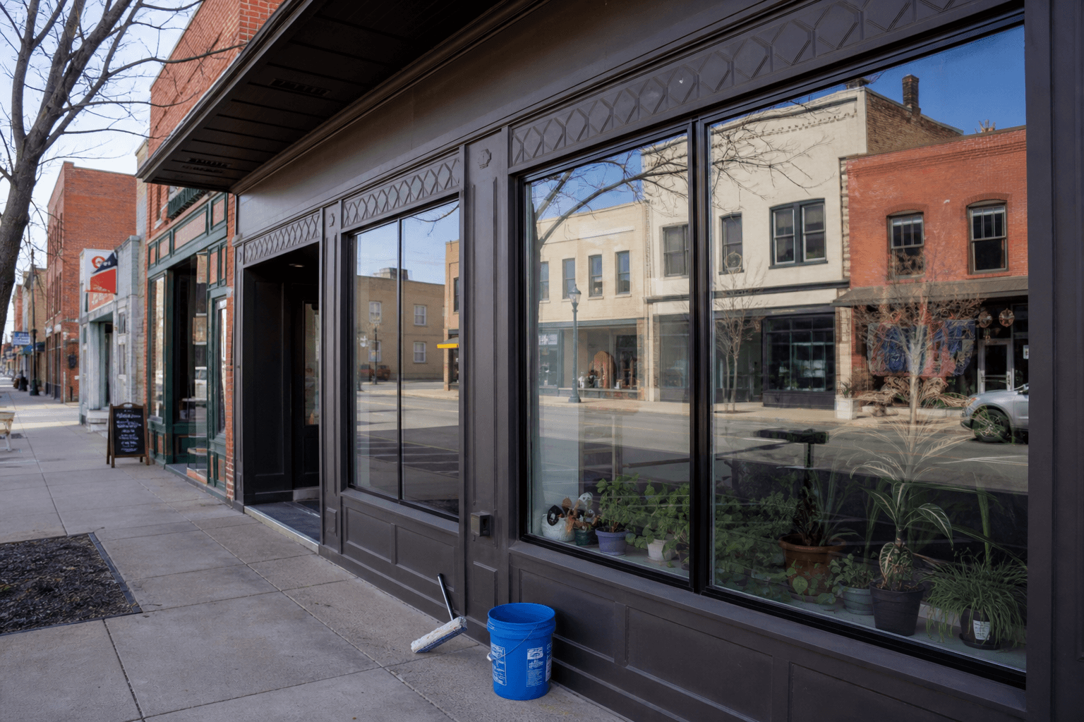 Ground-level wide view of retail storefront windows and squeegee bucket on pavement; no people